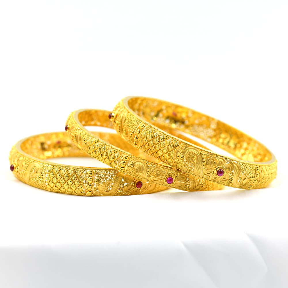 ornate gold bangles with intricate patterns and red stone accents